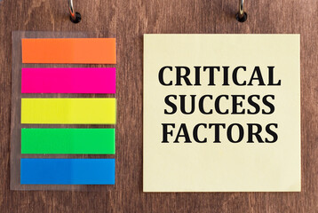 CRITICAL SUCCESS FACTORS text on yellow card on wooden background next to colored stickers pasted