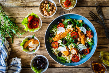 Tasty salad - fried chicken nuggets, chickpeas , bulgur groats, mini tomatoes and fresh green vegetables on wooden background
