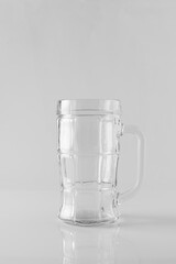 An empty glass beer mug on a white mirrored table. Light background, space for text