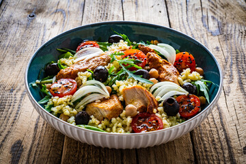 Tasty salad - fried chicken nuggets, chickpeas , bulgur groats, mini tomatoes and fresh green vegetables on wooden background
