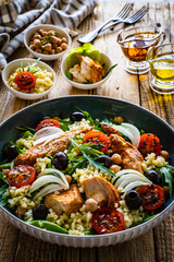 Tasty salad - fried chicken nuggets, chickpeas , bulgur groats, mini tomatoes and fresh green vegetables on wooden background
