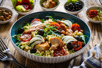 Tasty salad - fried chicken nuggets, chickpeas , bulgur groats, mini tomatoes and fresh green vegetables on wooden background
