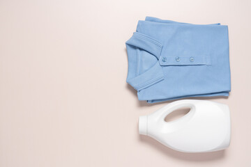 White bottle of detergent and stack of clean blue cotton shirts on beige background. Laundry and dry cleaning service concept