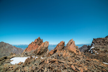 Scenic mountain landscape with old rocks and stones among snow in sunlight. Awesome alpine scenery with stone outliers on high mountain under blue sky in sunny day. Sharp rocks at very high altitude.