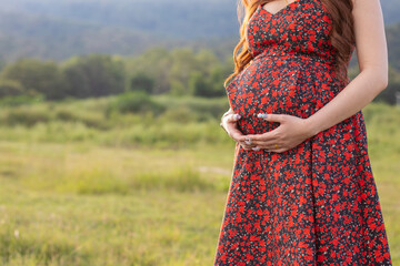 A pregnant woman nearing birth, wearing a vintage floral red maternity dress, is standing and grabs...
