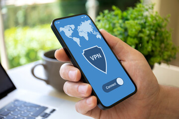 male hand holding phone with app vpn over table laptop