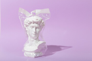  Fake sculpture of David's head in a plastic bag on a lilac background. Surreal ecology concept, copy space for text