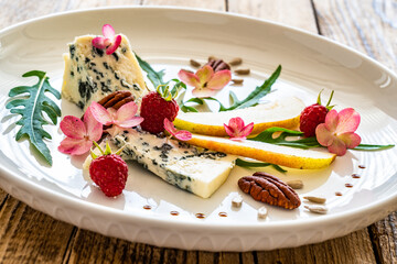 Fresh salad - blue cheese, raspberries, pear, arugula and pecan nuts on wooden background

