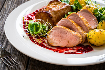 Fried pork loin with boiled potatoes and fresh vegetables on wooden table

