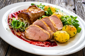 Fried pork loin with boiled potatoes and fresh vegetables on wooden table
