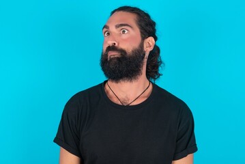Fototapeta premium young bearded man wearing black T-shirt over blue studio background making grimace and crazy face, screaming out of control, funny lunatic expressing freedom and wild.
