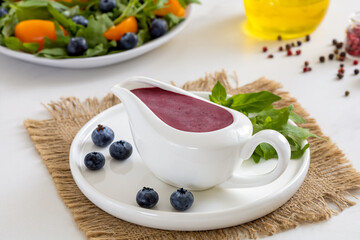 Blueberry sauce. Berry Vinaigrette Salad Dressing made with fresh blueberries, oil, balsamic vinegar, honey, salt and pepper served in white ceramic gravy boat. 