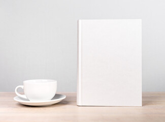 Obraz na płótnie Canvas Book mockup and cup at wooden table. Reading leisure, relaxation with tea or coffee mug, harmony concept. Novel, encyclopedia, code template with empty cover.