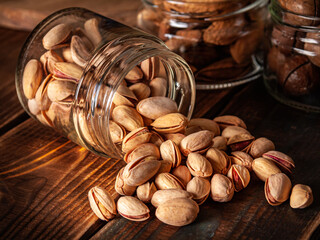 Upside down transparent jar with pistachios, on a wooden dark brown table, warm shade. Horizontal....