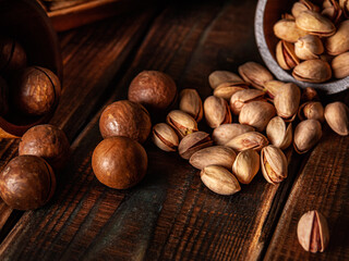 A scattering of macadamia nuts and pistachios on a dark brown wooden background. Selective focus. Low key. Advertising poster. Art. Brown and coffee tones. Horizontal