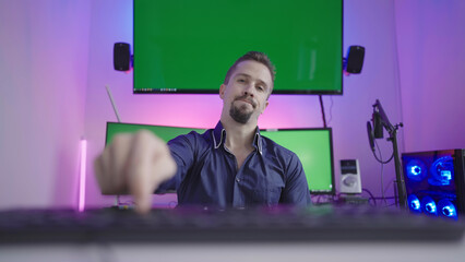 Bored man pushing keyboard button repeatedly with green screens in back