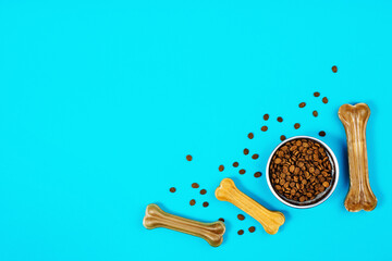 Dry dog pet food in bowl and accessories on blue background top view. Pet feeding and care concept background with copy space. Photograph taken from above.