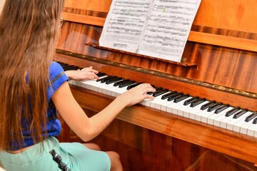 The girl plays the piano according to the notes at the music school.