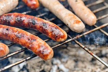 Grilled juicy sausages cooked on a campfire outdoors.