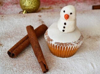 Christmas composition: Christmas cupcakes decorated with icing and surrounded by cinnamon sticks and star anise on a background of powdered sugar