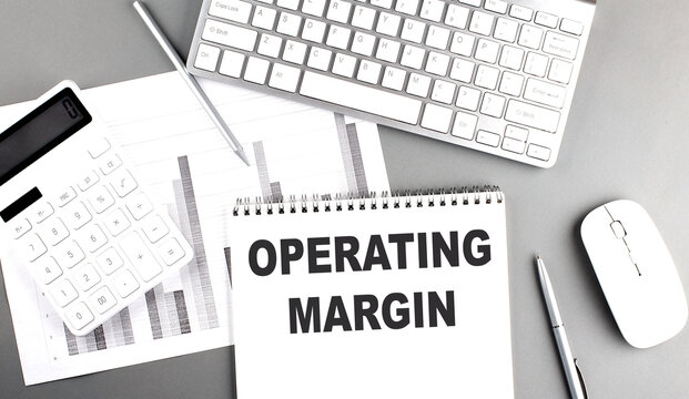 OPERATING MARGIN text written on notebook on grey background with chart and keyboard, business concept