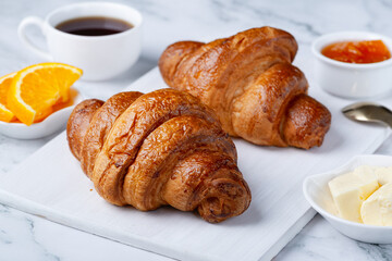 Fresh sweet croissants with butter and apricot jam for breakfast. Continental breakfast on a white concrete table