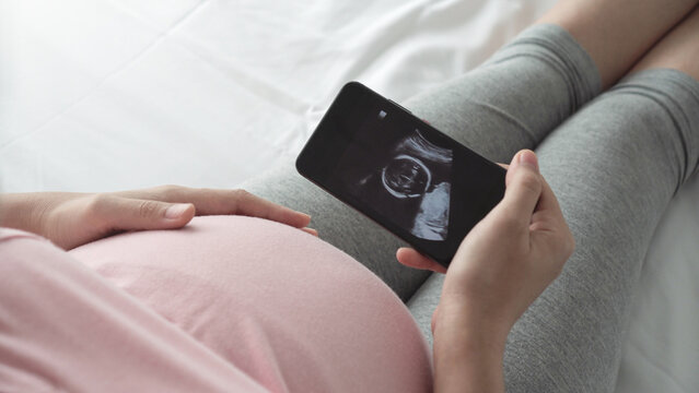 Female waiting her baby, Pregnant woman looking her ultrasound scan photo on Smartphone. Concept of pregnancy, Maternity prenatal care.