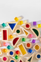 Fototapeta na wymiar Wooden blocks with translucent rainbow stones on white background. Colorful toys for Kids. Educational game for toddler. Play with light and exploring coloured shadows.