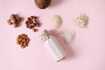 Flat lay food composition with a plant based milk and wholesome nuts, cereals and seeds on pink background. Copy space