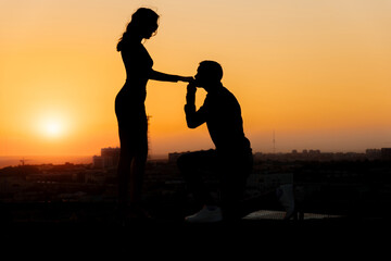 Fototapeta premium Couple in love kissing against the backdrop of an orange sunset. Dark silhouettes of a man and a woman