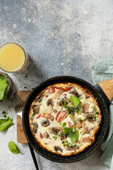 Italian breakfast dish. Rustic omelette (frittata) with mushrooms and bacon on a cast iron pan. View from above. Copy space.