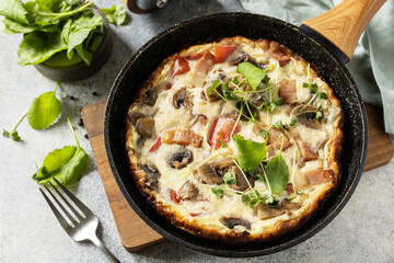 Rustic omelette (frittata) with mushrooms and bacon on a cast iron pan. Italian breakfast dish.