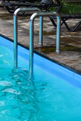 Descent to a bright blue pool with clear water and wooden formwork. Steel railing of the stairs in the pool with blue water. Entrance to the pool