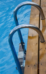 Descent to a bright blue pool with clear water and wooden formwork. Steel railing of the stairs in the pool with blue water. Entrance to the pool