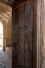 Entrance to ancient religious building with brick walls and carved wooden door, Bukhara, Uzbekistan