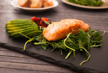 Baked sea trout fillet with fresh vegetables and herbs on black board