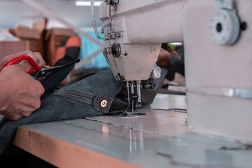 A seamstress cuts fabric while working at a sewing machine in the workshop. Women's hands
