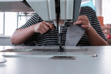 A seamstress cuts fabric while working at a sewing machine in the workshop. Women's hands