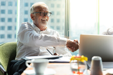 Picture of two business man discussing business and seem like an agreement is made. The young man is wearing white shirt with black tie. The older man is wearing black suit. They meet in hotel lobby.