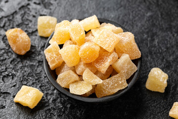 Sweet and spicy candied ginger in black bowl on dark stone background