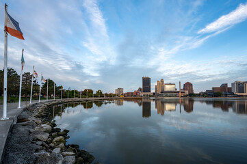 Reflection of downtown Toledo Ohio skyline during sunrise from international park with a leading line of flags - obrazy, fototapety, plakaty