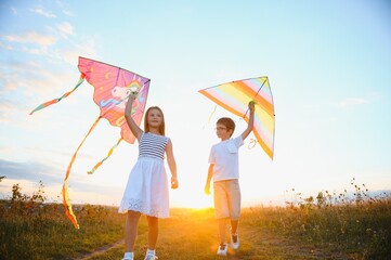 Happy children launch a kite in the field at sunset. Little boy and girl on summer vacation.