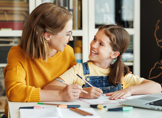 Cheerful mother doing homework with daughter at home