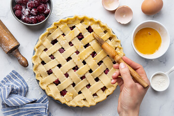 Preparation homemade  pie with cherry filling.  Female hand greases lattice top with whisked egg. Making pie series.