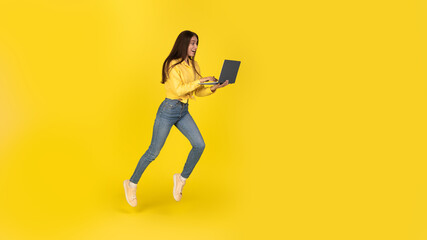 Excited Freelancer Woman Using Laptop Running In Air, Yellow Background