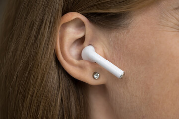 Wireless earphone object in female ear close up. Gadget user woman using white small earbud,...