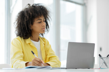 Focused millennial african american female student giving online class at home, taking notes in notebook, copy space, e-education