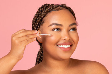 African American Lady Applying Facial Serum Moisturizing Skin, Pink Background