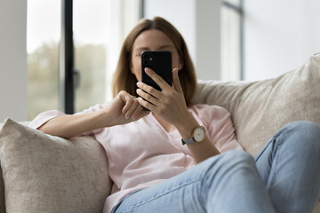 Young millennial unrecognizable smartphone user woman resting on home sofa, holding mobile phone, using online app, shopping on Internet, chatting. Communication