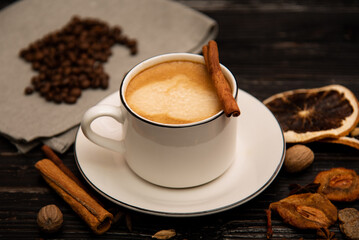 A mug of coffee on a wooden background with spices.